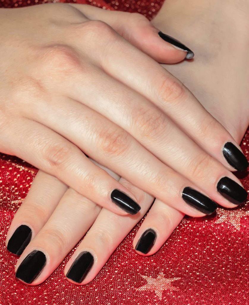 Two hands overlapping on a red cloth showing nails with black nail polish